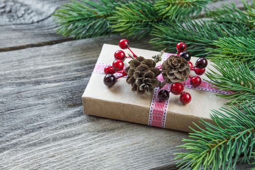 Christmas composition of pine cones, spruce branches and gift box with fir cones and holly berries on the background of old unpainted wooden boards; with copy-space