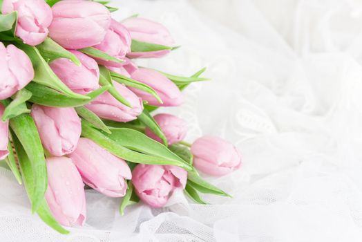 Bouquet of fresh pink tulips flowers covered with dew drops are on lacy textile close-up