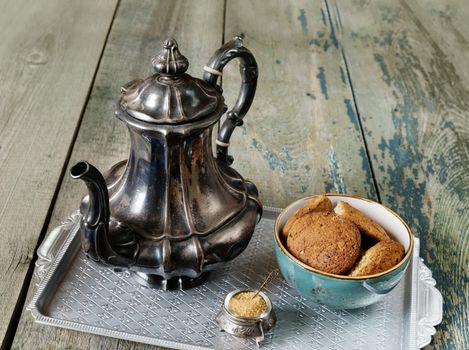 Beautiful antique silver coffee pot and oatmeal cookies in an old old blue ceramic bowl are on a old dark wooden boards