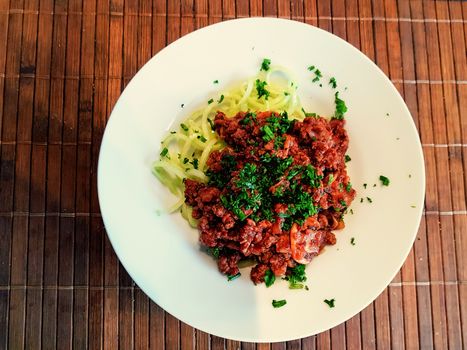 Healthy low carb food on white plate, lunch with snake cucumber in spaghetti strips cut above beef tartare with tomato sauce.