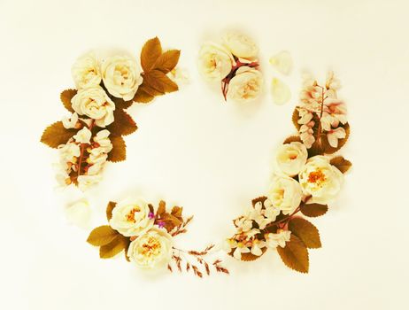 Decorative frame in retro style consisting of white wild rose flowers with green leaves on white background. Top view, flat lay. Toned image