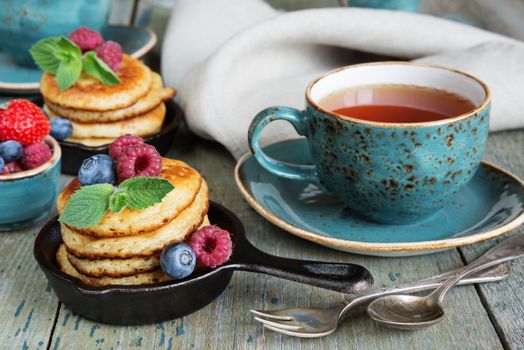 Breakfast of pancakes, fresh raspberries, blueberries and black tea in blue ceramic vintage cup, in rustic style