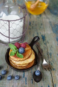 Breakfast of pancakes in cast-iron frying pan, fresh berries honey and milk in rustic style