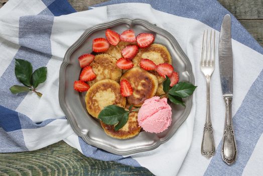 Summer breakfast of pancakes with ice cream and ripe berries of strawberry on an antique tin plate, with vintage knife and fork, top view