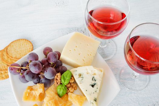 Two glasses of red wine, different varieties of cheese, walnuts, red grapes and basil leaves, top view