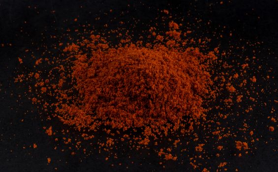 Pile of red paprika powder isolated on black background, top view