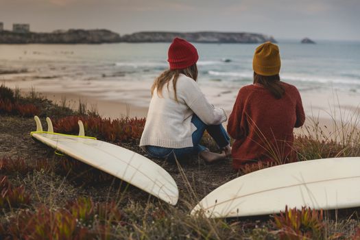 Two best friends sitting near the coastline with her surfboards while looking to the ocean