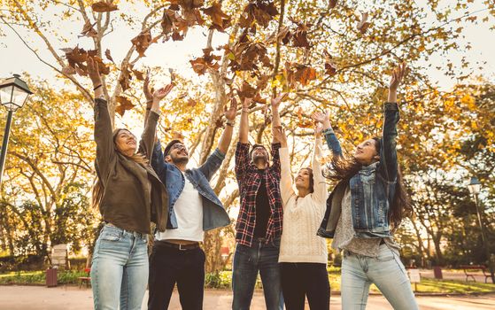 Group of friends in the park having fun throwing leaves in the air