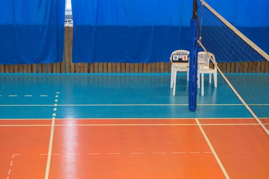 An empty gym with a volleyball net, chairs and display Board in the school.