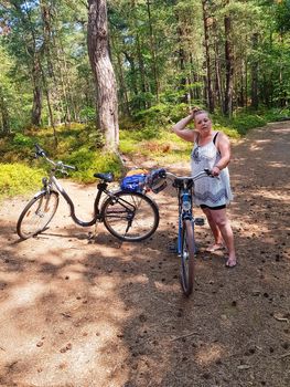 Older carefree woman rides a bike through the woods in summer