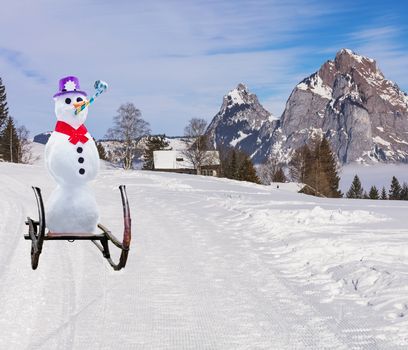 funny christmas concept of a party snowman wearing a hat and roller tongue sliding down the ski hill slope on a sleigh