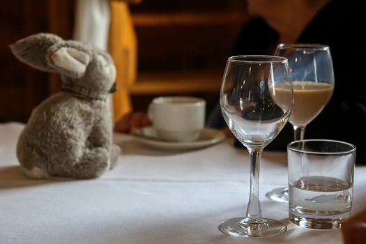 Glass with Irish creme liqueur, empty glass, glass with water, cofee cup and rabbit on the table.