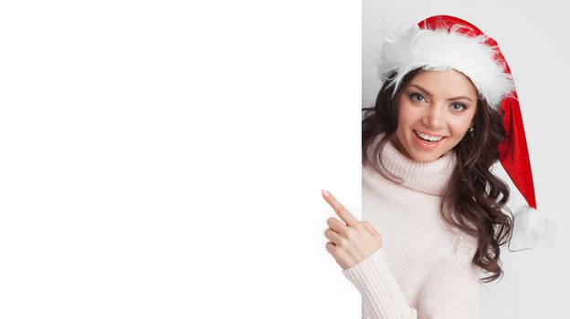 Portrait of happy girl with Christmas hat holding poster and pointing to copy space