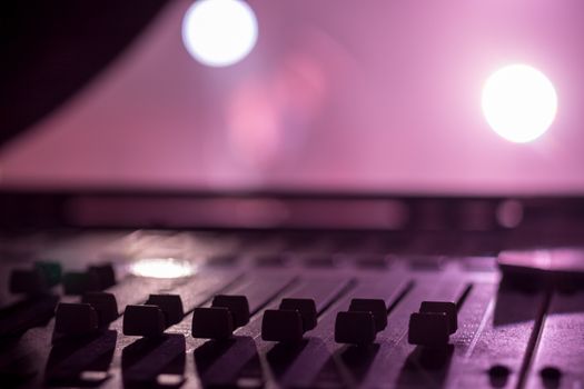 Stage side Low level view of Faders on a Professional Audio Sound Mixing Console at music festival, black Faders and pink purple background