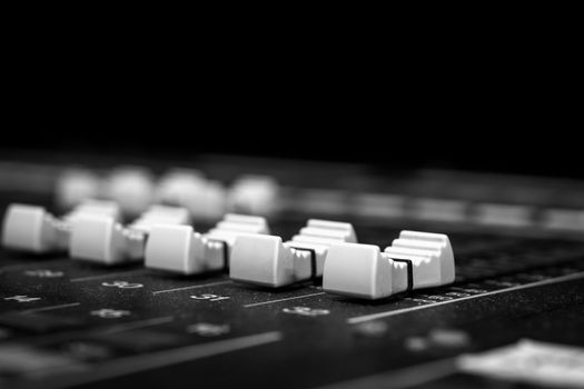 Low level view of 5 Faders on a Professional Audio Sound Mixing Console at music festival, black desk and white Faders