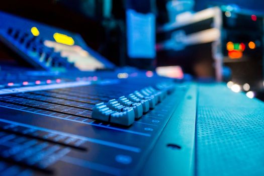 Low level view of a professional audio mixing console with rack equipment in the background