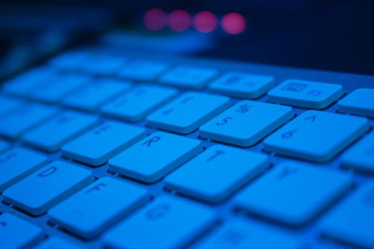 Closeup of a computer keyboard in blue light with 4 leds in the background