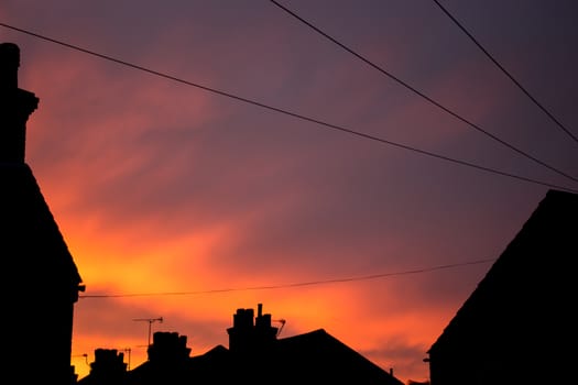 Dark silhouette roof tops in urban british city with orange and purple sky in the background