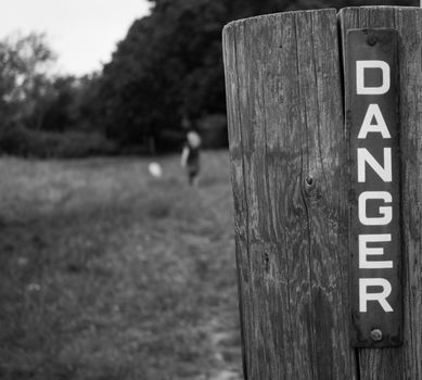 Metal danger sign on wooden gate post with blurred figure in background