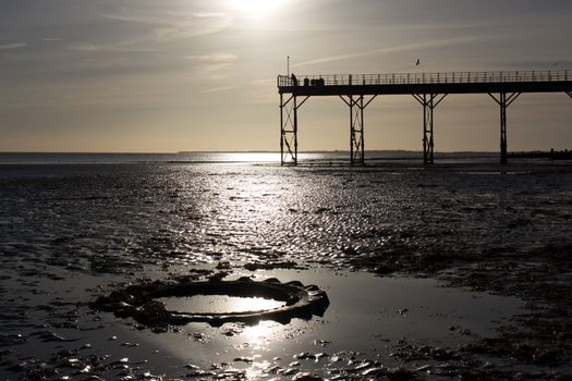 low tide warm sunset, man stood on old english victorian pier with tractor tyre in foreground