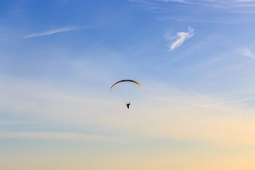 Single Powered paraglider with red and yellow canopy in blue sky and soft wispy clouds