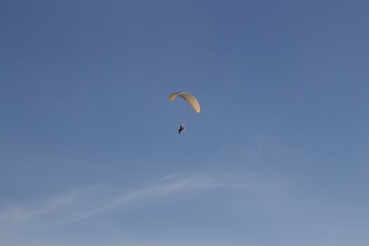 Single Powered paraglider with red and yellow canopy in blue sky and soft wispy clouds