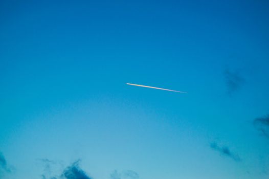 The trace of the plane on the background of a beautiful blue sunset in the sky.