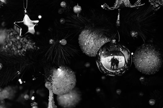 Black and white picture of some Chistmas tree ornaments. A couple of friends appear reflected on a ball.