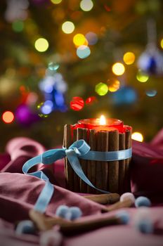 Christmas candle on the background of branches of  Christmas tree and luminous garlands. Burning candle in front of Christmas Tree.