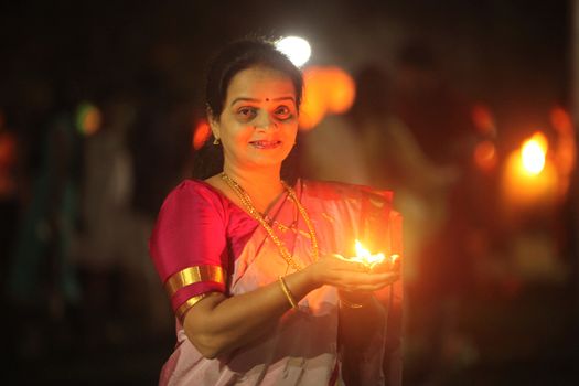 Pune, India - November 2018: A woman lights up a lamp during a public celebration of Diwali festival before sunrise, in India.