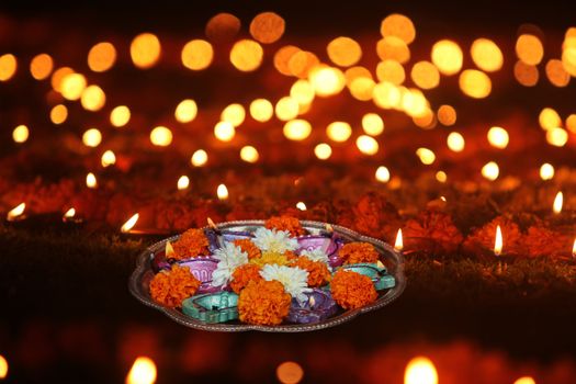 A plate of lamps and marigold flowers for hindu ritual kept on a lawn with other lamps, during Diwali festival in India.