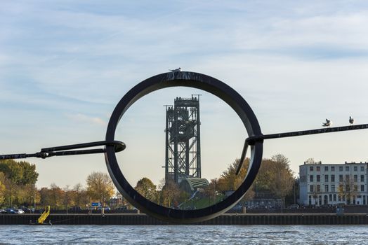 an old railroad bridge in rotterdam seen througt a metal circle over the water the meuse