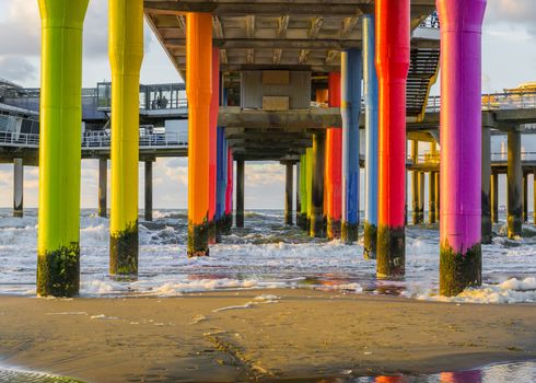 Rainbow colored stone poles under the pier of scheveningen beach the netherlands with sand and waves in the in the sea