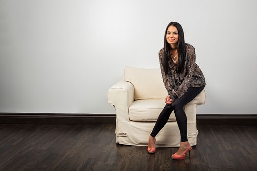 Trendy wenty something woman, sitting on the arm of a couch, with big smile