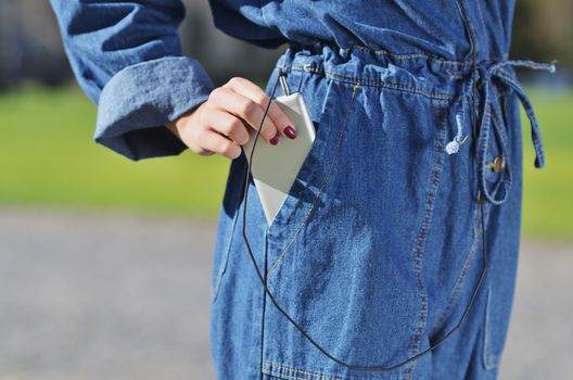 A girl in a denim suit pulls out a smartphone to listen to music. spring Sunny day the warmth
