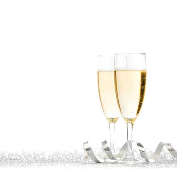 Glasses of champagne and silver ribbons on glitter background