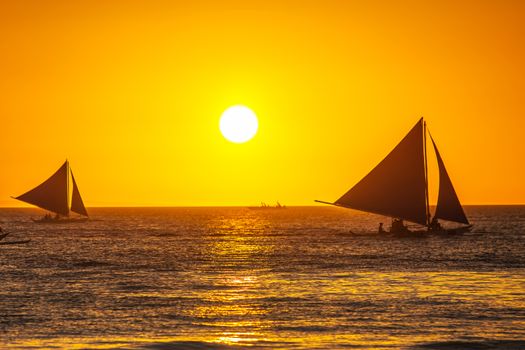 Sailboats in open tropical sea at sunset