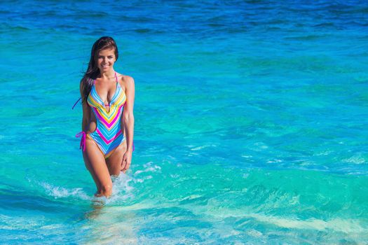Beautiful slim woman in bikini walking in sea waves
