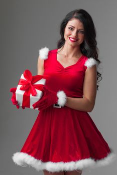 Beautiful young woman in Santa dress celebrating Christmas holding gift box