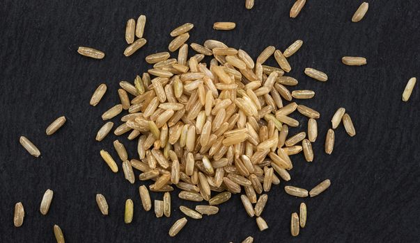 Heap of brown rice groats on black background, top view