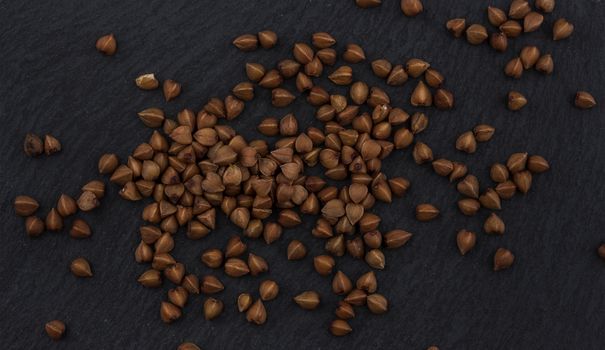 Heap of buckwheat grain on black background, top view