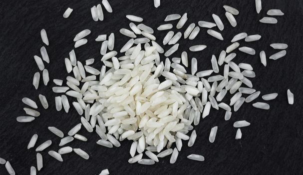Heap of rice grains on black stone background, top view