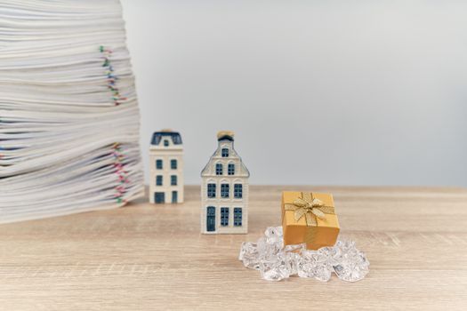 Golden gift box on ice have blur house and stack of overload paperwork report on wooden table with white background and copy space. Business and finance on happy new year and merry christmas concept. 