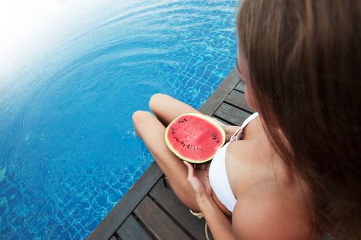 Girl holding watermelon sitting by the blue swimmin pool