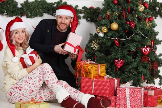 Couple in love sitting next to a nicely decorated Christmas tree, holding Christmas gifts and smiling