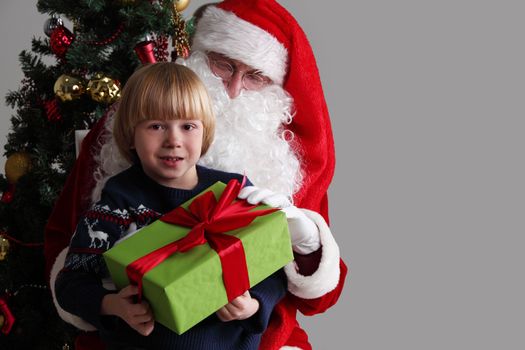 Portrait of smiling little boy sitting on santa claus knees and getting a gift