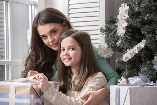 Mother and daughter unwrapping a gift sitting on the floor near christmas tree