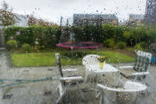 glass window with water raindrops looking in the garden with blurry effect autumn background