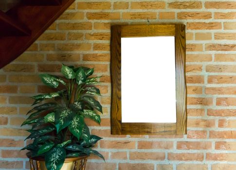 empty blank cut out wooden mirror or painting frame hanging on a brick wall in a room decorated with a house plant