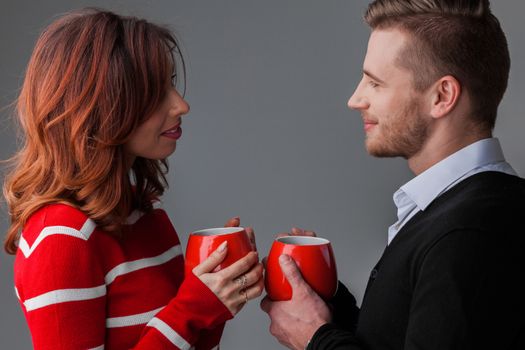 Beautiful young couple in love looking to each other holding red cups , Valentines day concept